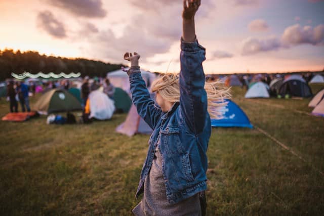 a woman raising her arms in the air in front of tents at summer camp