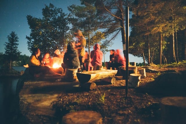 group of people near bonfire near trees during nighttime at summer camp